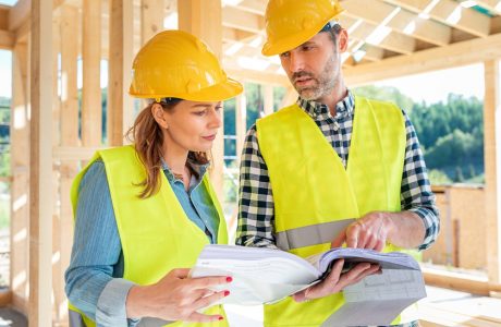 Engineers working on construction site holding blueprints of wood frame house